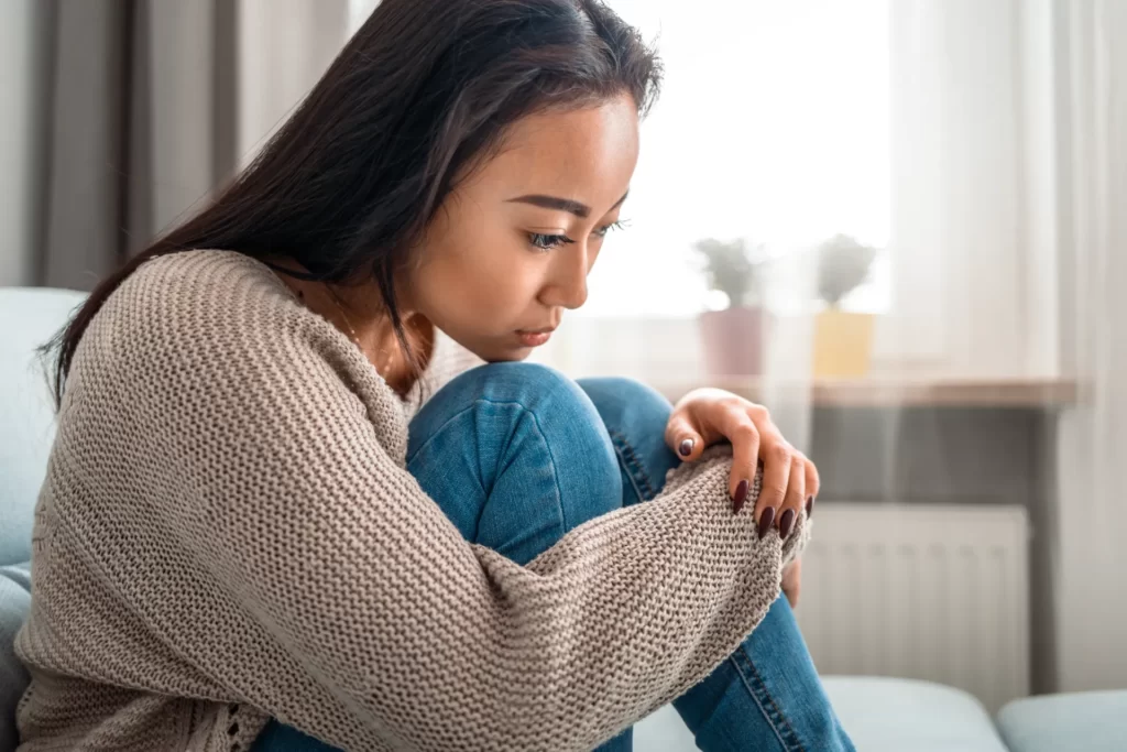 pensive woman embracing knees indoors by bright w utc